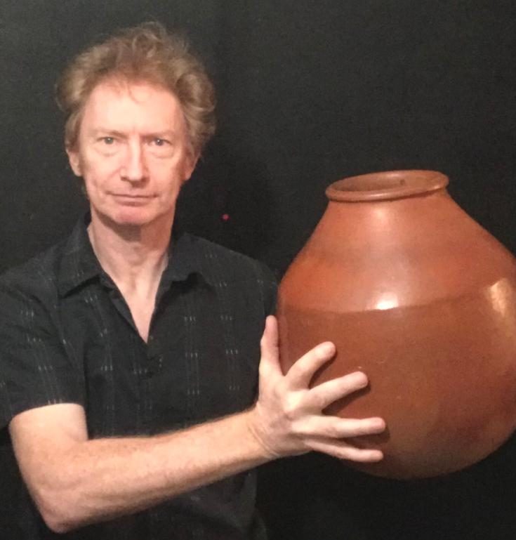 Homme tenant un grand pot en argile sur fond noir.